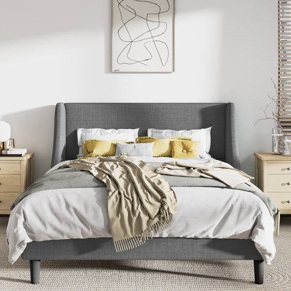 Gray upholstered bed with white bedding and yellow pillows in a bedroom setting.