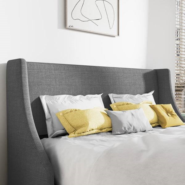 Gray upholstered bed with yellow and gray pillows against a white wall.