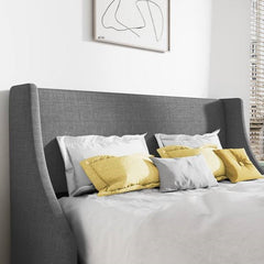 Gray upholstered bed with yellow and gray pillows against a white wall.