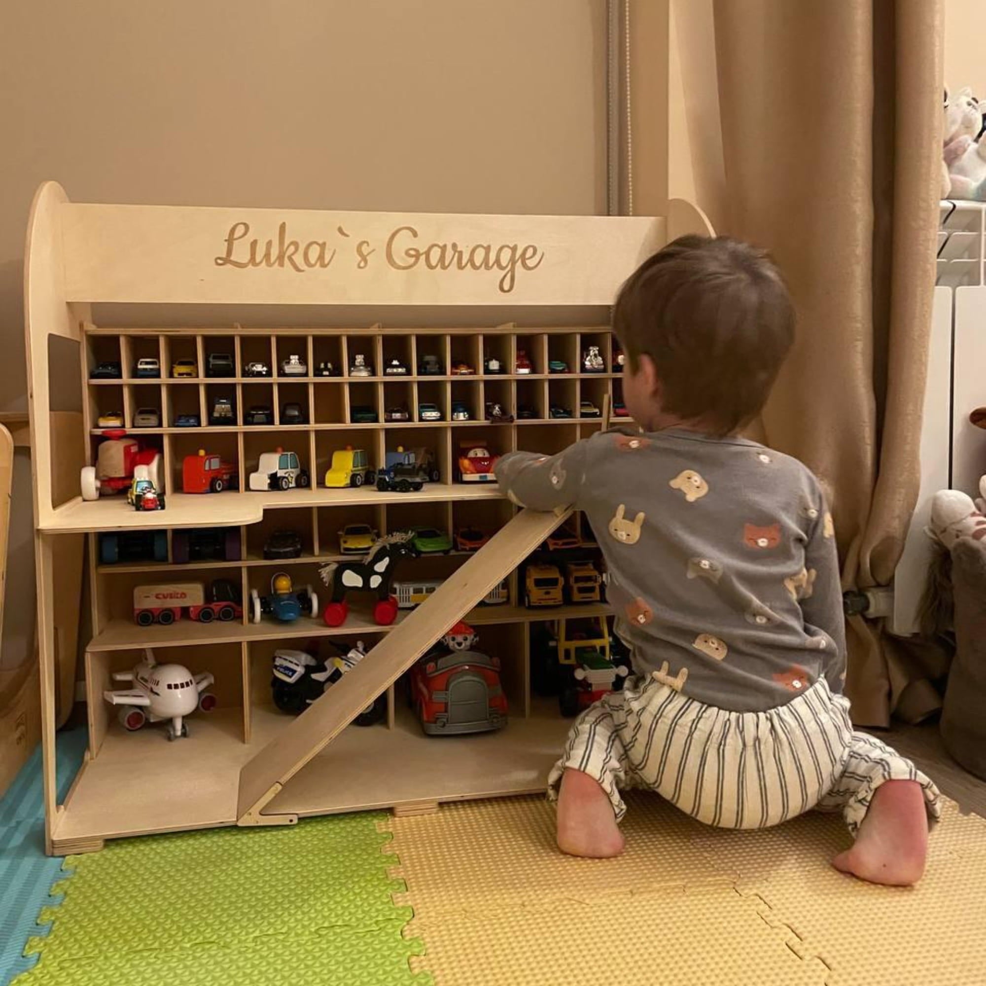 Child playing with a toy garage set up with various toy cars and trucks.