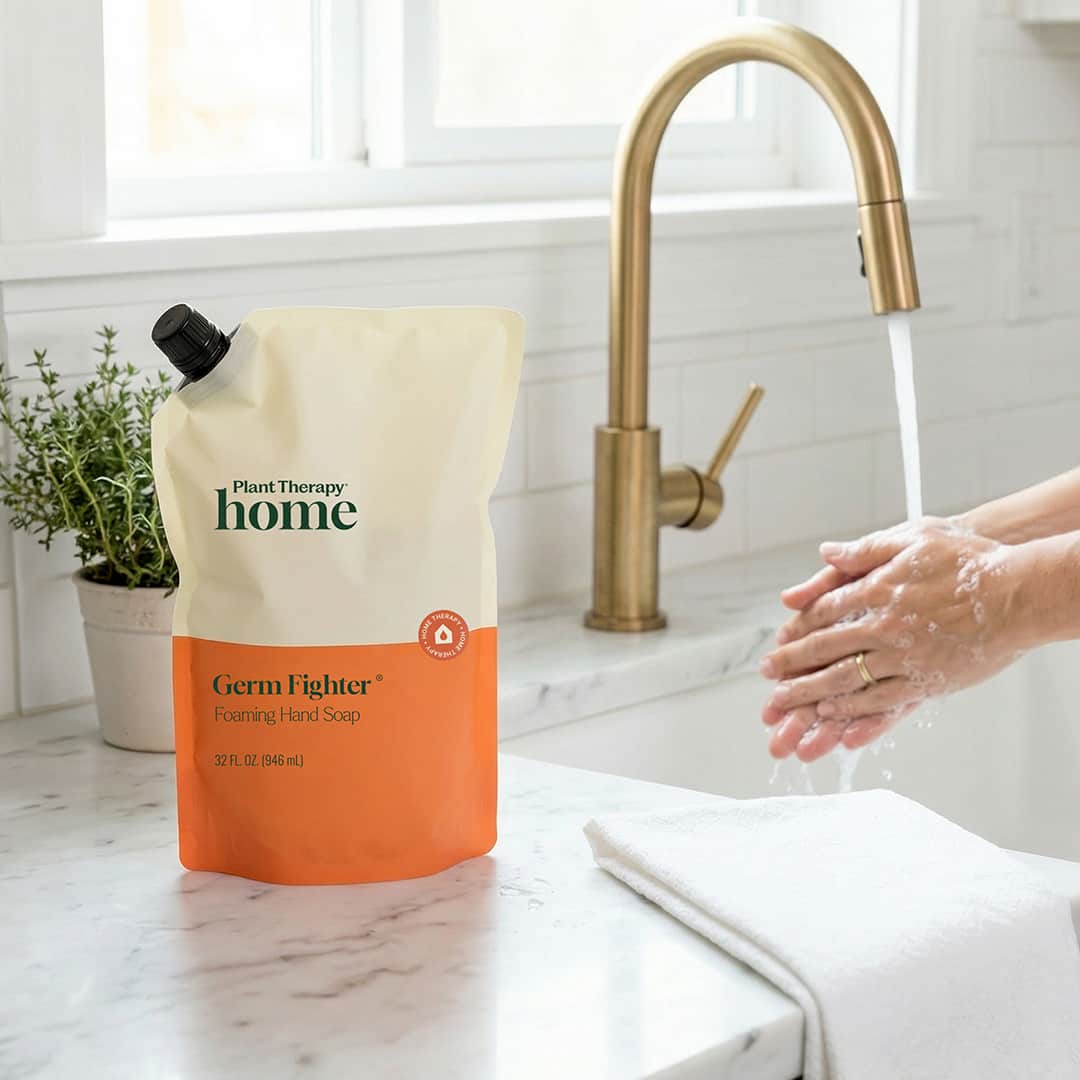 Bag of 'Burt's Bees Home' Germ Fighter hand soap on a kitchen counter with hands washing in the sink.