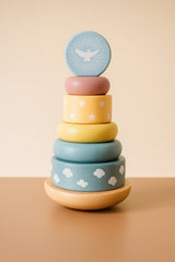Stack of colorful wooden rings with cloud and dove designs on a beige background