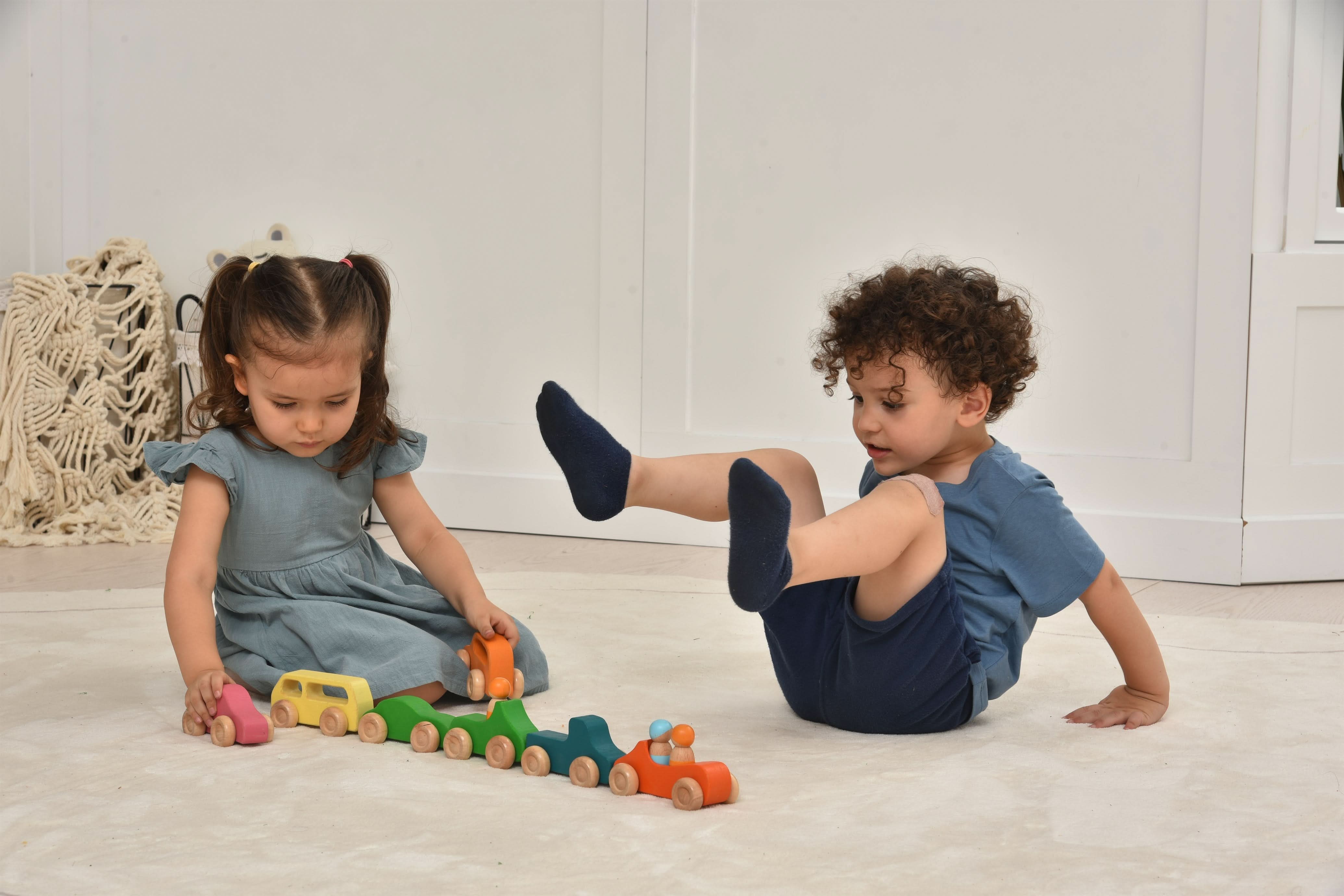 Two children playing with colorful wooden toys on a light-colored floor.