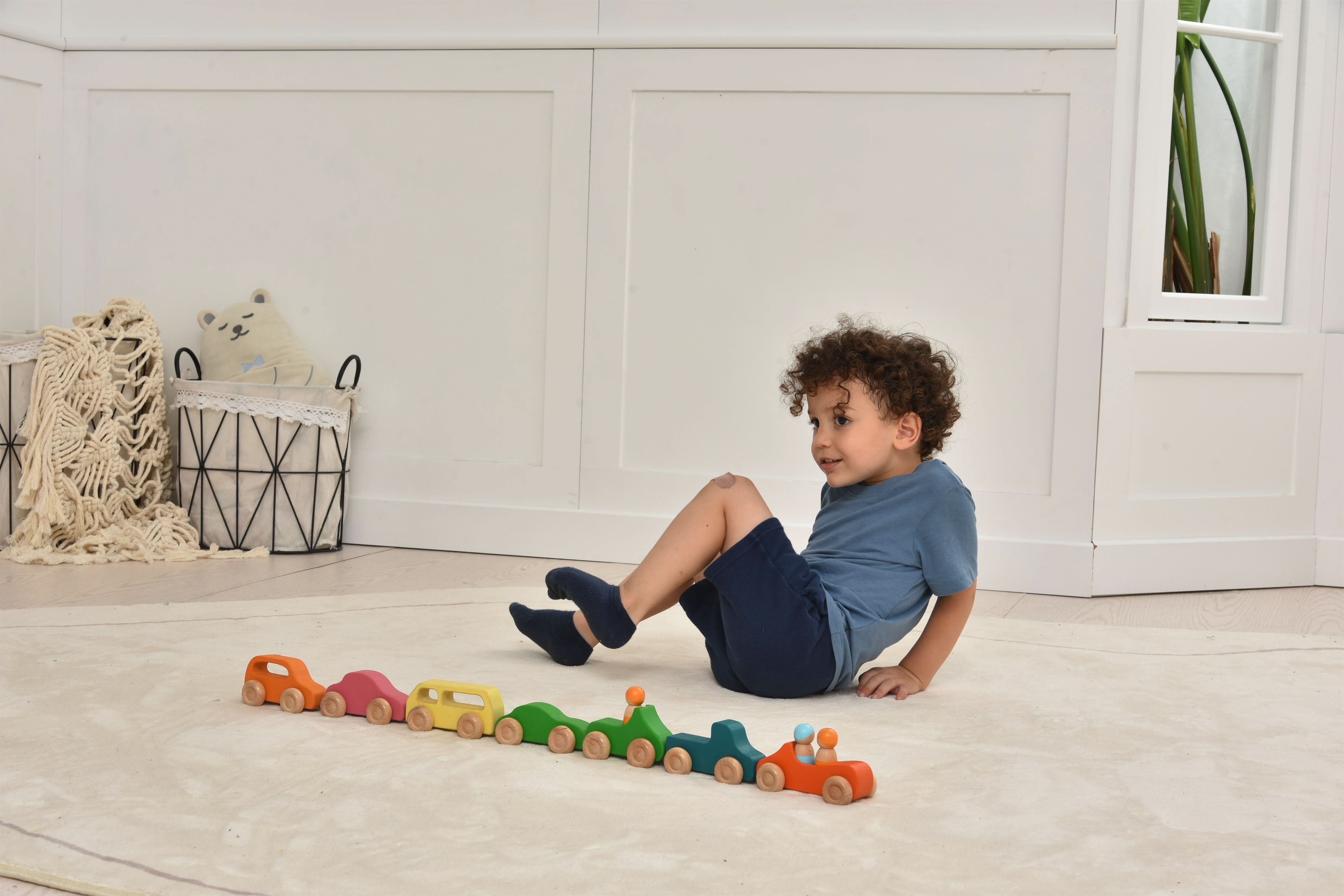Child playing with colorful wooden toy cars on a light wood floor.
