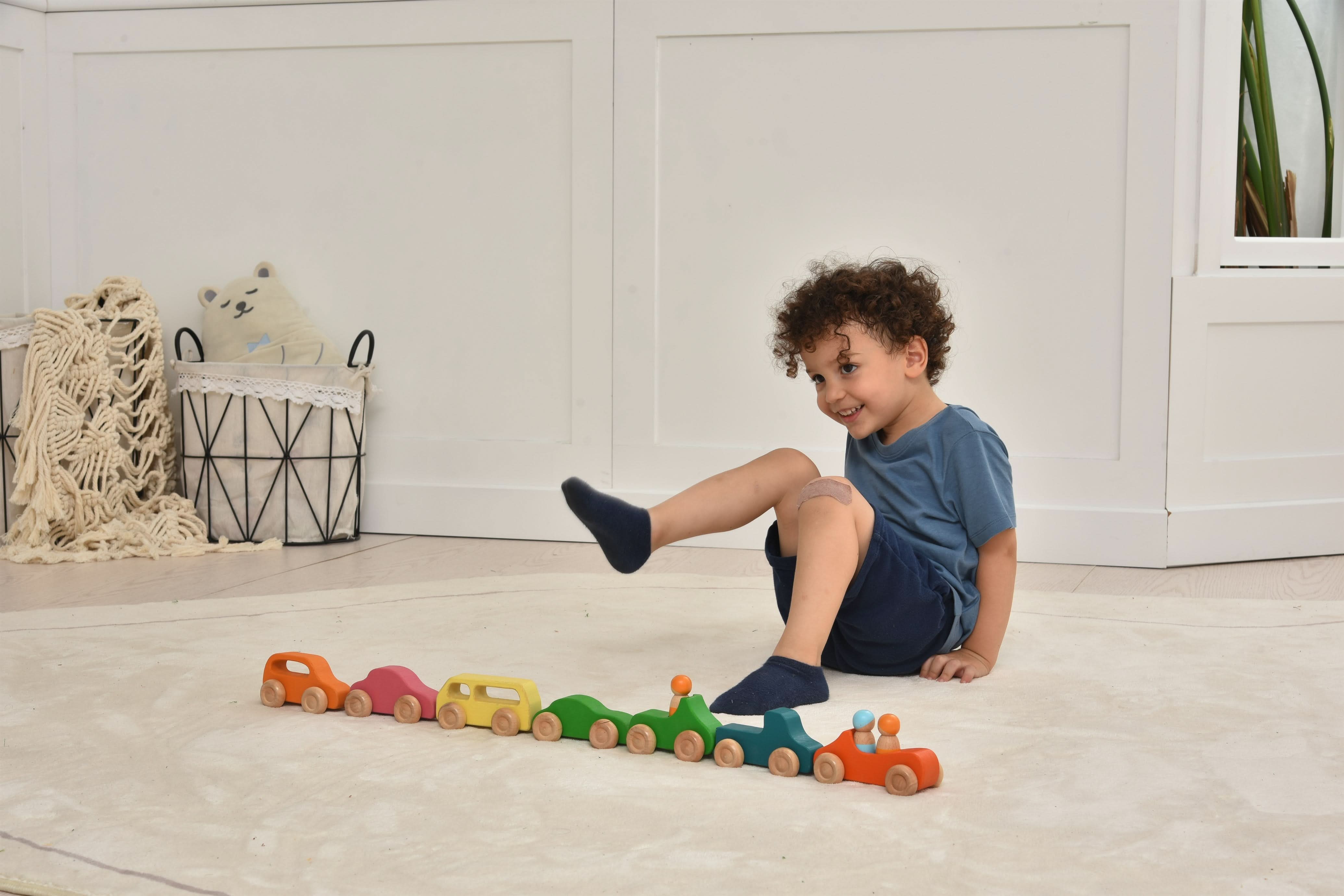 Child playing with a colorful wooden toy train on a light wood floor.