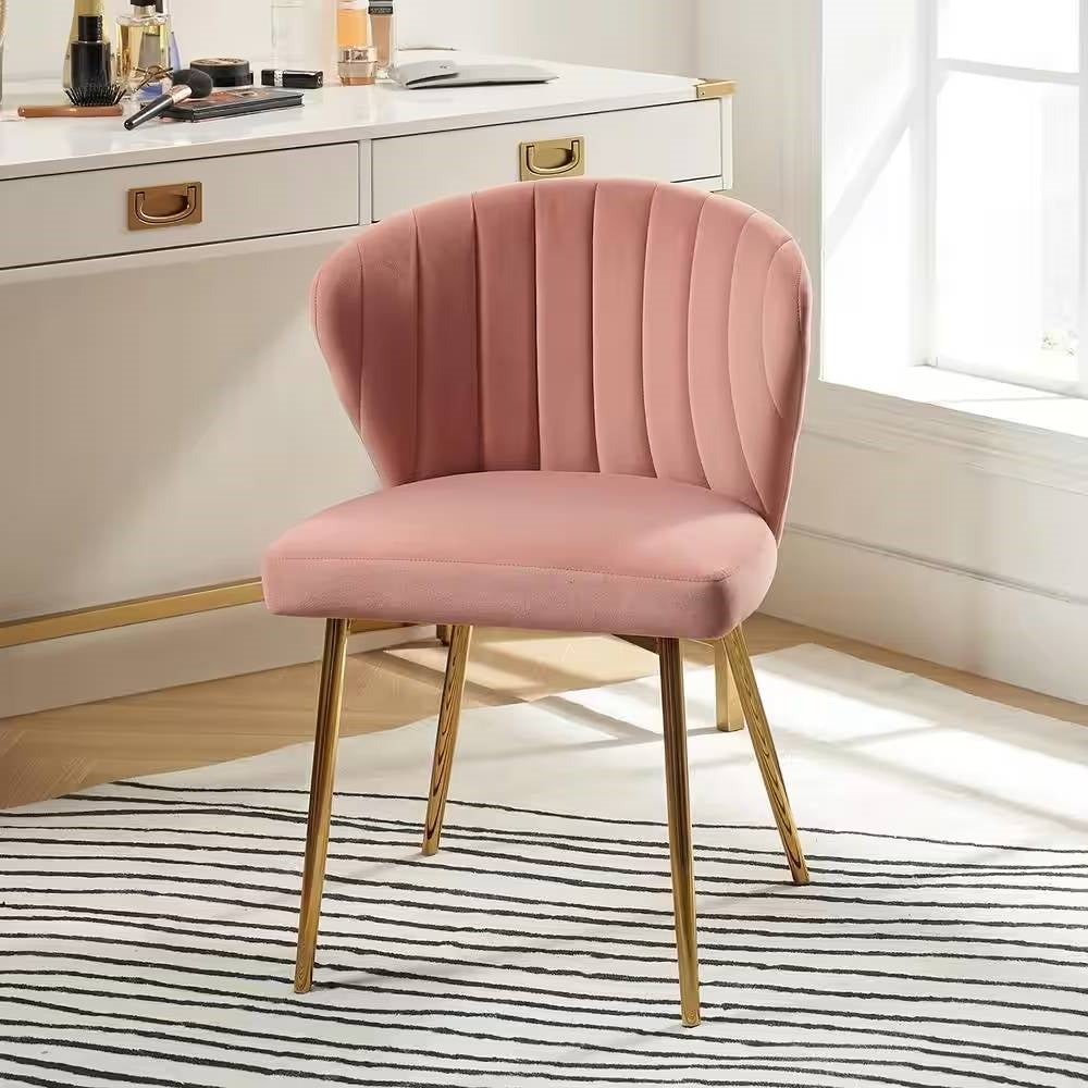 Pink velvet chair with gold legs in a room with a desk and window.