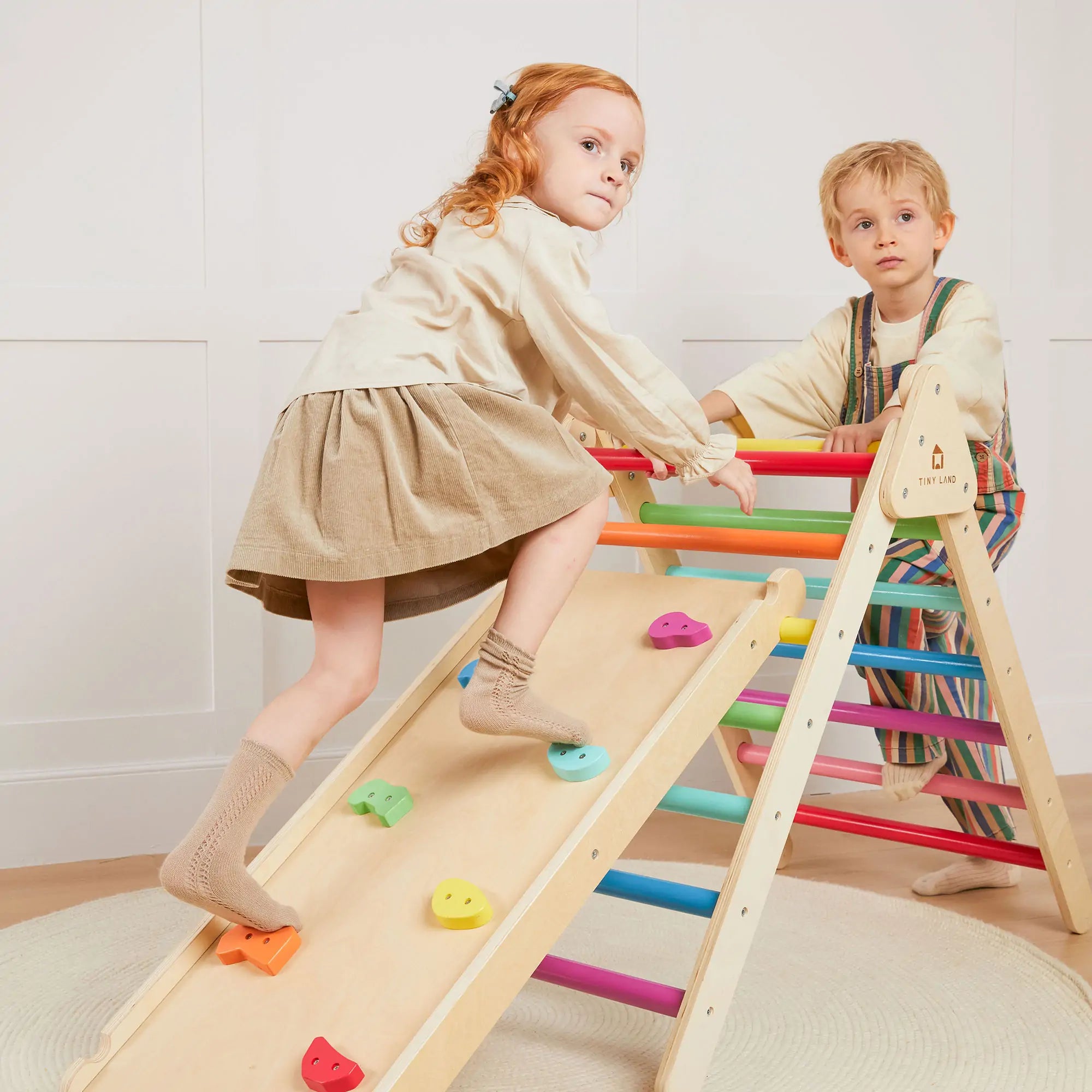 Two children playing on a colorful wooden climbing toy indoors.