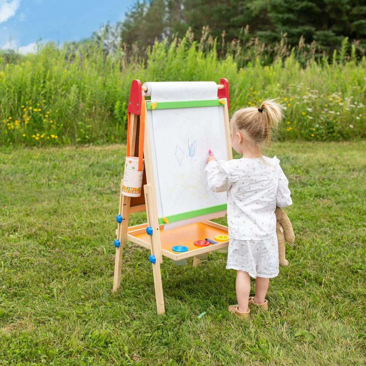 Child drawing on easel outside in the grass 