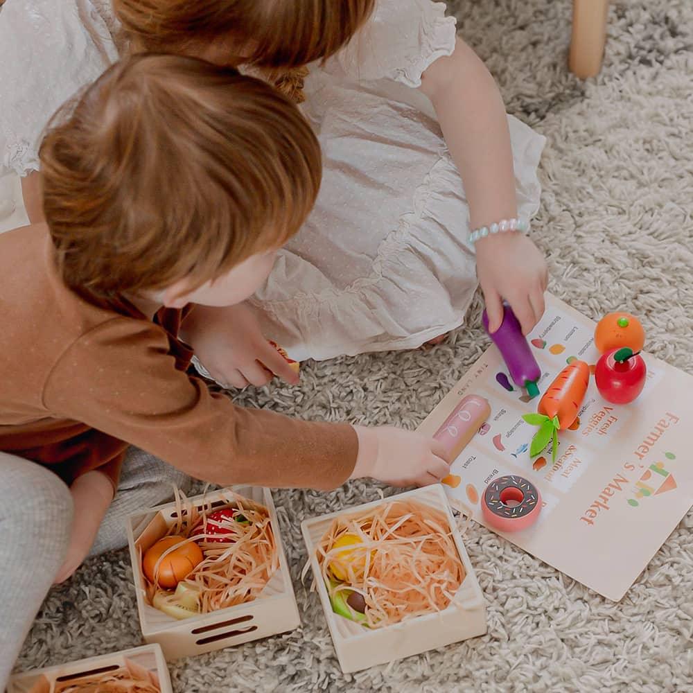 Two children playing with toy fruits and vegetables on a carpeted floor.