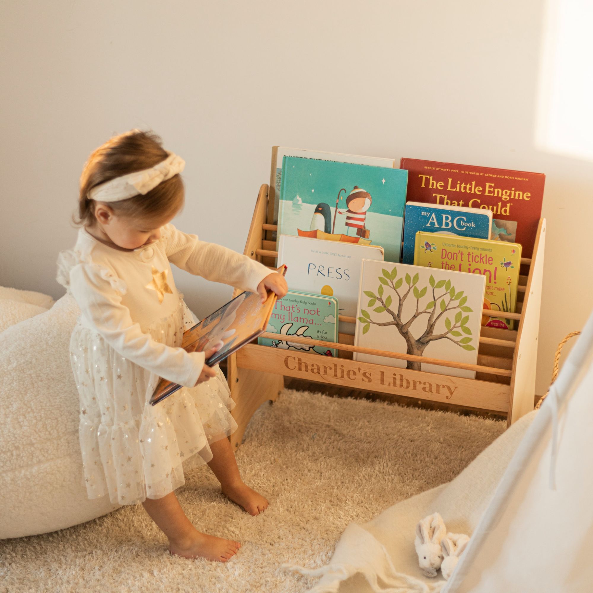 Child in a white dress sitting on the floor with a bookshelf of children's books.