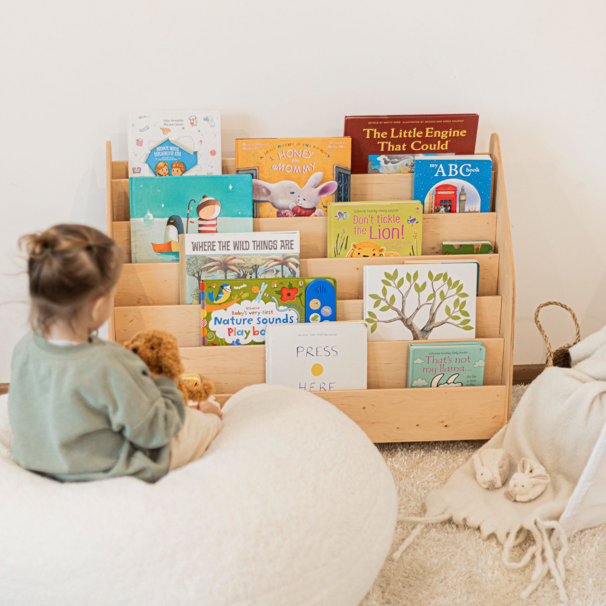 Child sitting on a bean bag chair reading books from a wooden bookshelf.