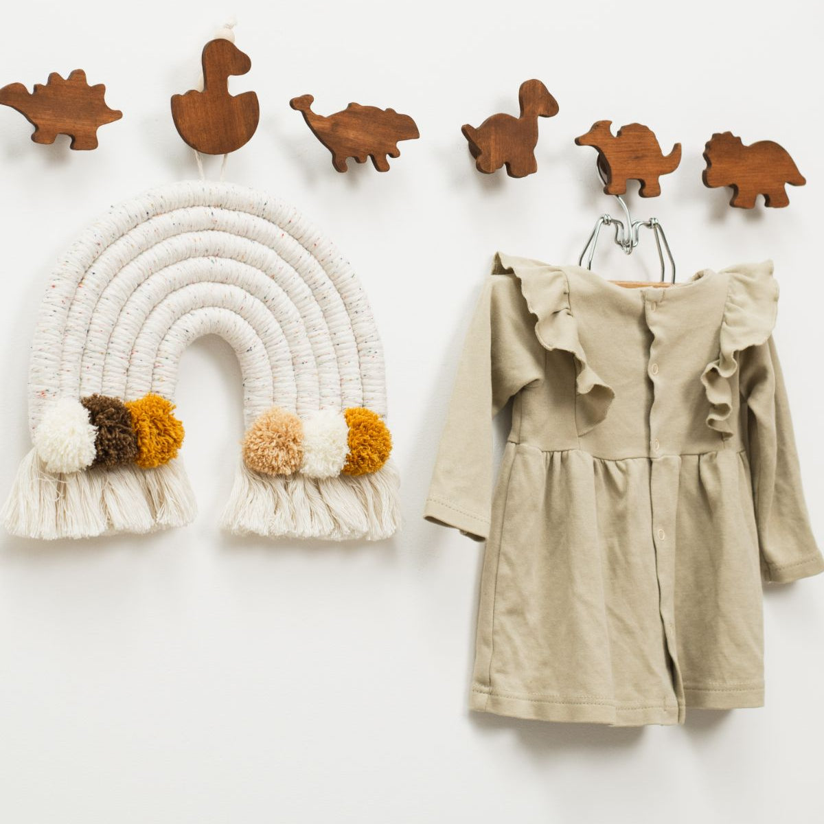 Children's dress hanging on a hook next to wooden dinosaur toys and a rainbow wall decoration.
