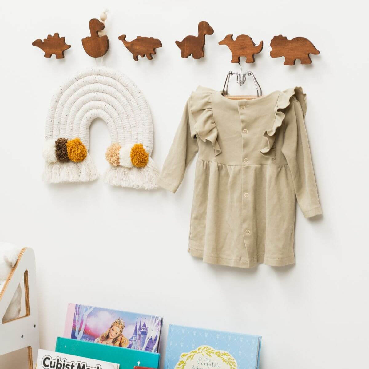 Children's dress hanging on a hook with dinosaur-shaped hooks above and books below.