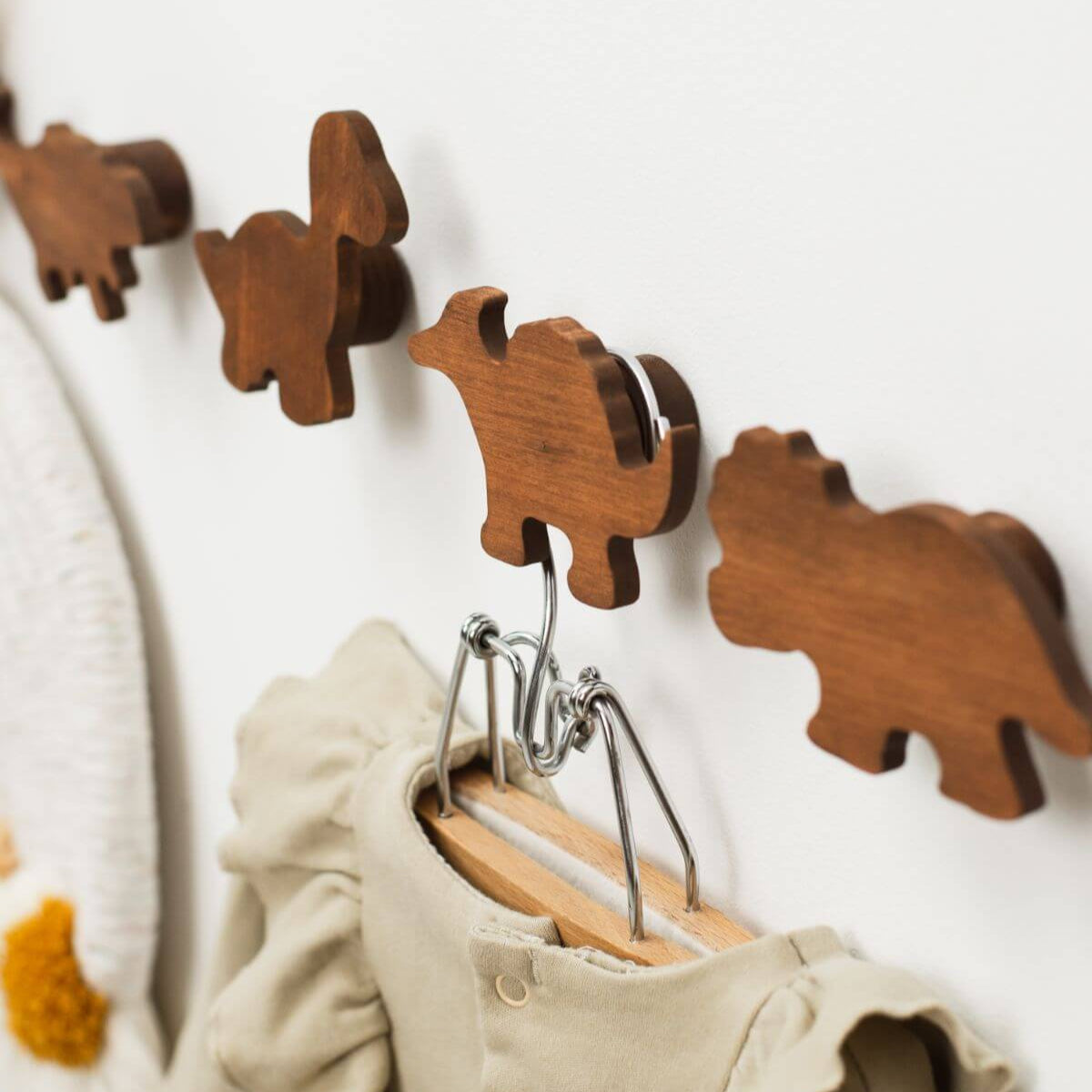 Wooden animal-shaped hooks on a white wall with baby clothes hanging from them.