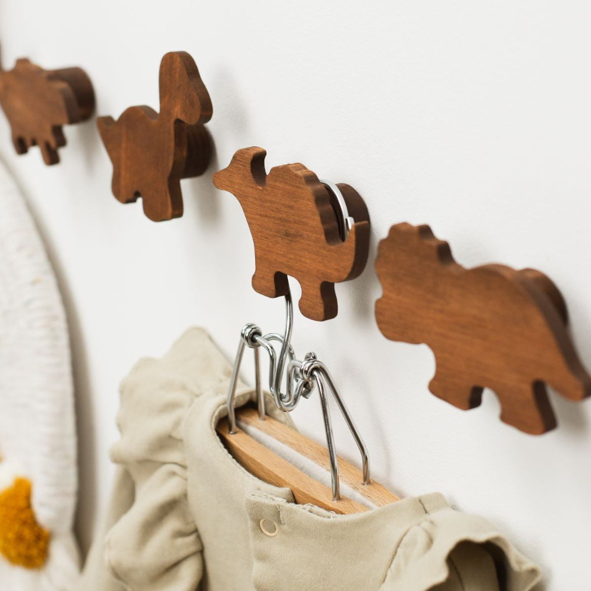 Wooden bear-shaped hooks on a white wall with clothes hanging from them.
