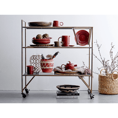 Decorative cart with red ceramic items against a white wall