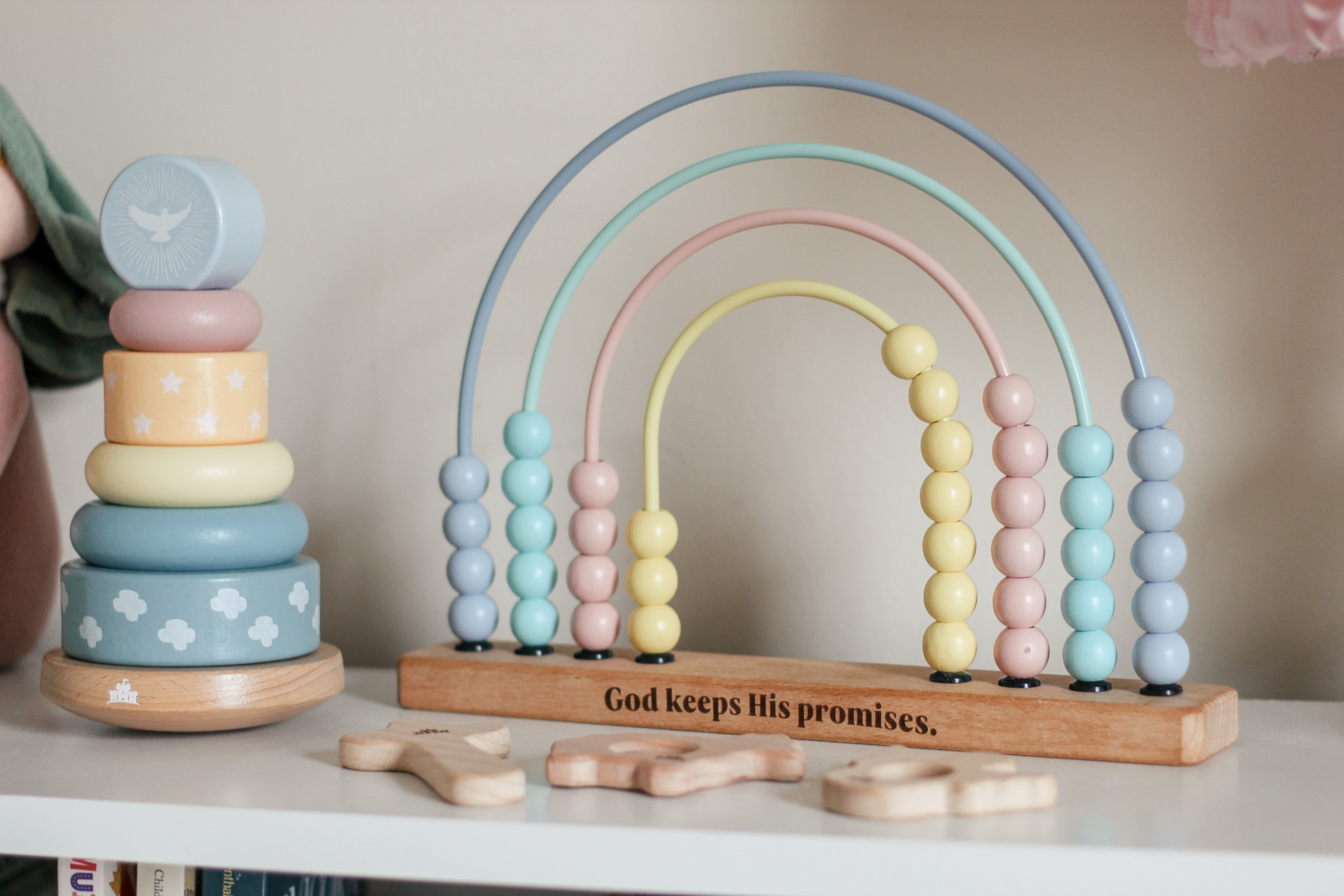 Pastel-colored wooden toys including a stacker and rainbow abacus on a shelf.
