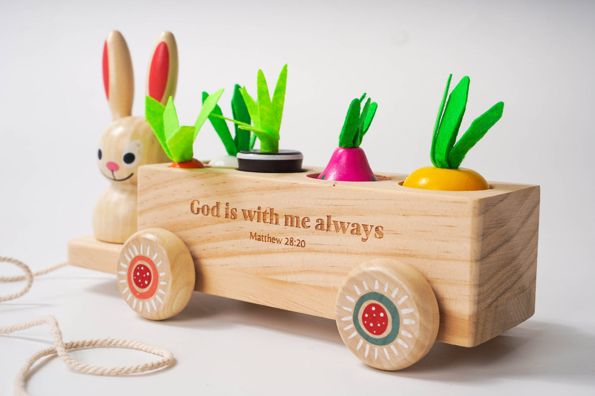 Wooden toy cart with rabbit figure and Easter vegetables, featuring the text 'God is with me always' on a light background.