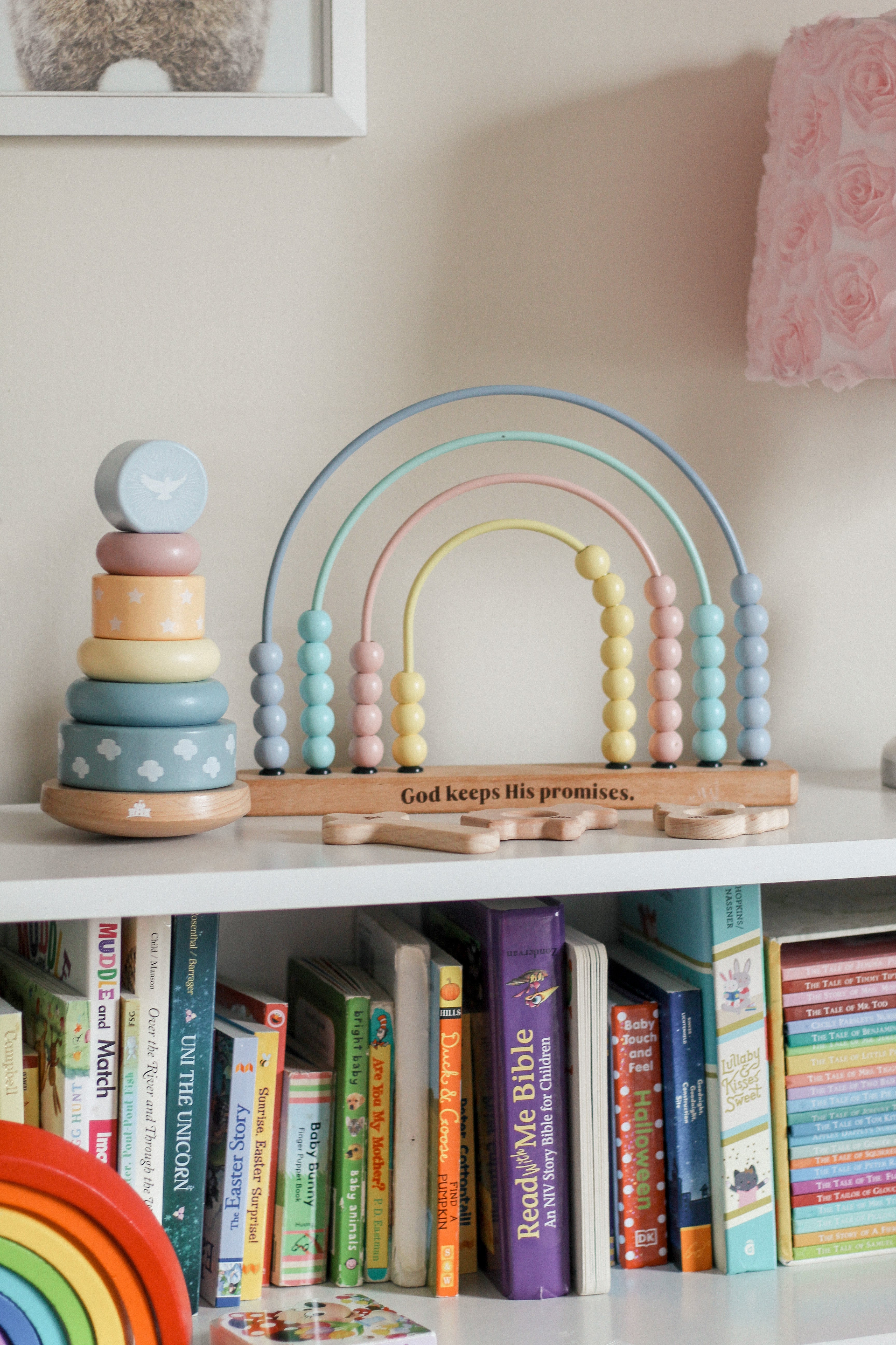 Pastel wooden rainbow arch and stacker toys on a shelf with books