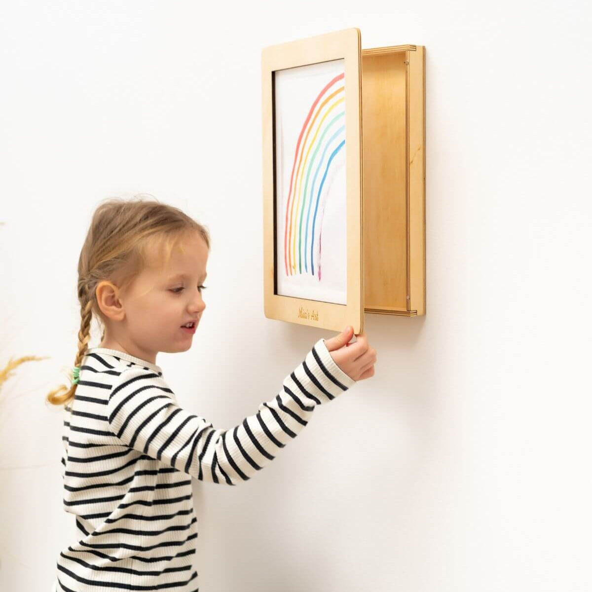 Child interacting with a wooden picture frame on a wall