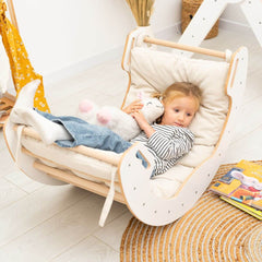 Child in a baby swing holding a plush toy in a cozy room.