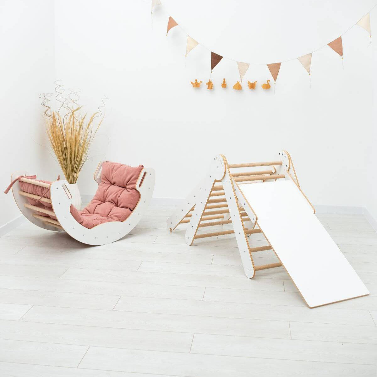 Children's indoor play area with a pink cushioned chair and wooden slide on a white floor.