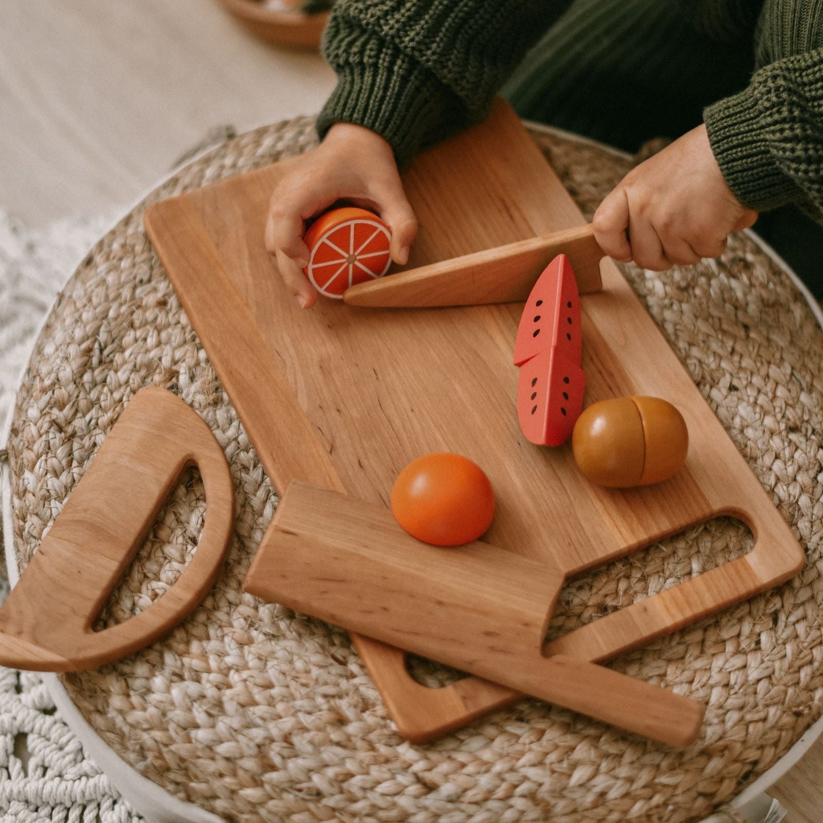 Person cutting a grapefruit on a wooden cutting board with fruit-shaped cutters on a woven surface.