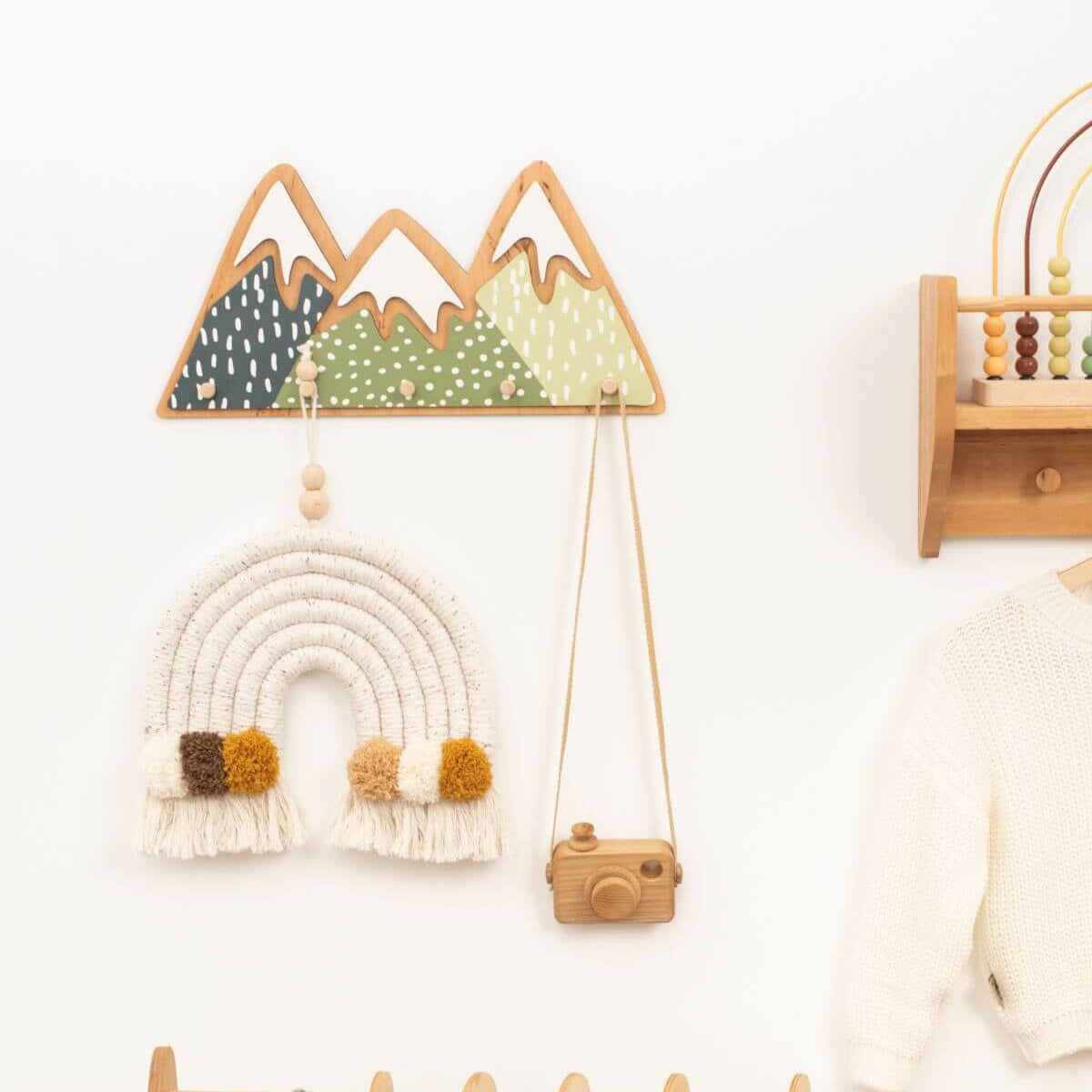 Decorative wall hanging with mountains, rainbow, and camera on a white wall.