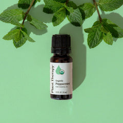 Bottle of Plant Therapy Organic Peppermint essential oil with mint leaves on a green background