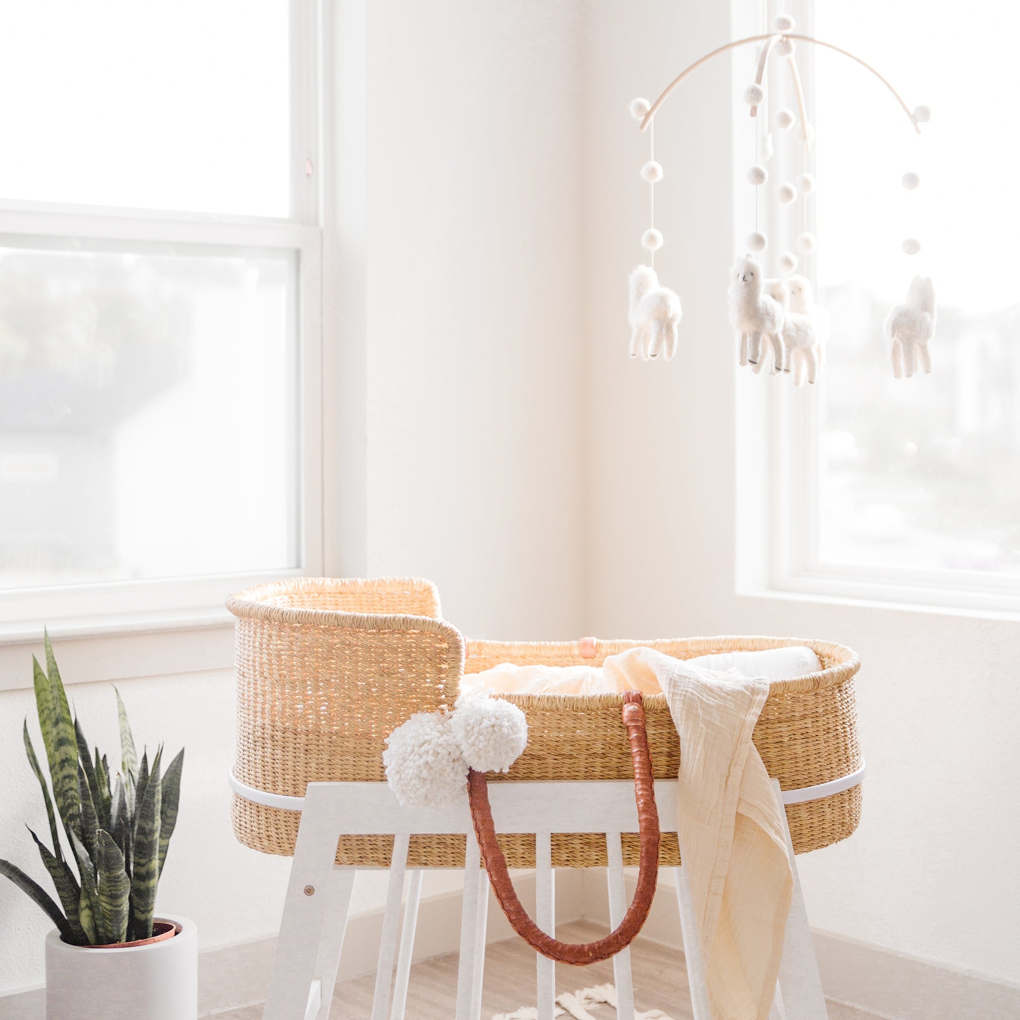Nursery room with a wicker crib, white stool, and hanging mobile.
