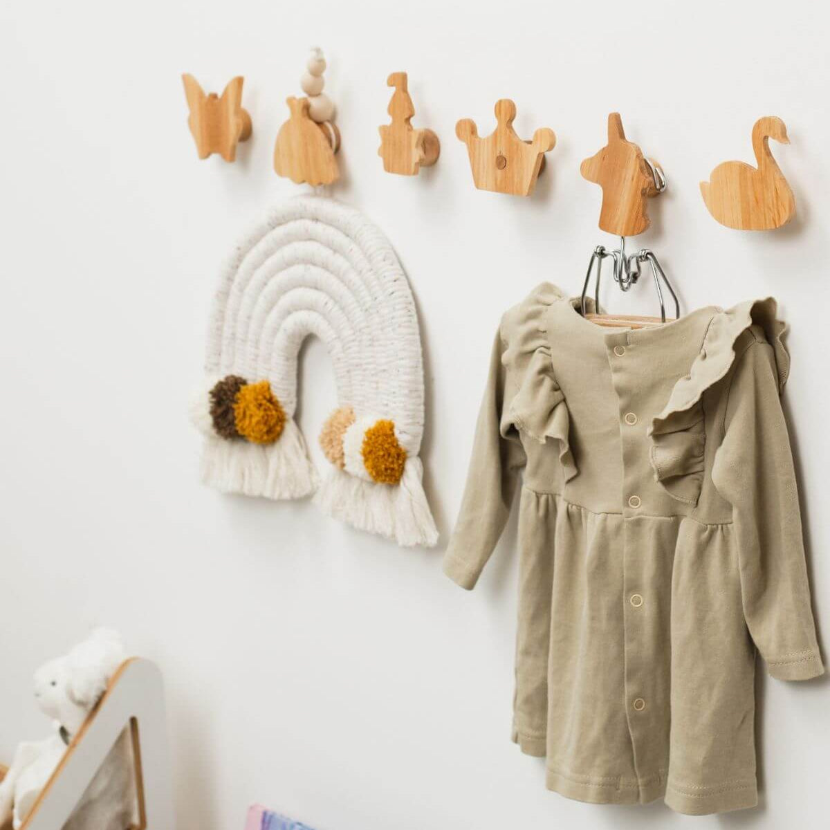 Children's dress hanging on a rack with wooden hooks and decorative items on a white wall.