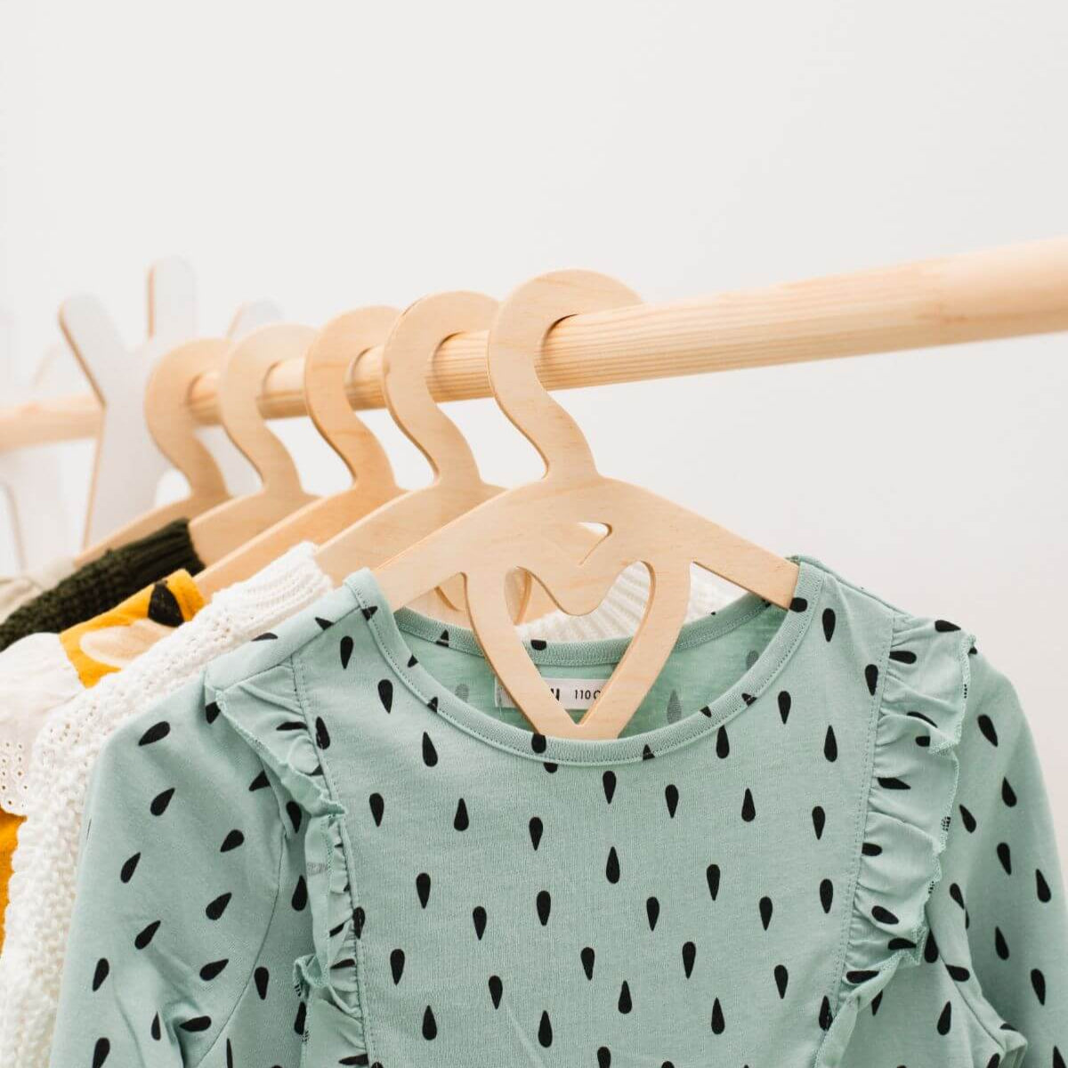 Green children's shirt with black patterns on a wooden hanger against a white background