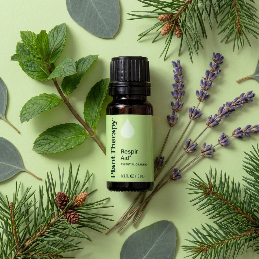 Essential oil bottle labeled 'Respir Aid' surrounded by green leaves, lavender, and pine branches on a light green background.