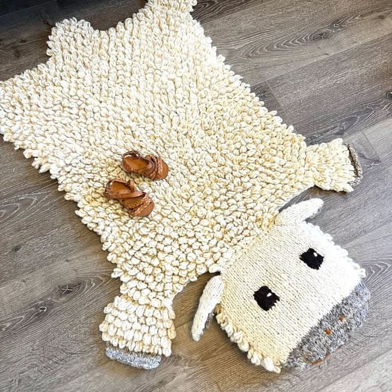Organic wool sheep nursery rug on white background showing hand-knit texture and design