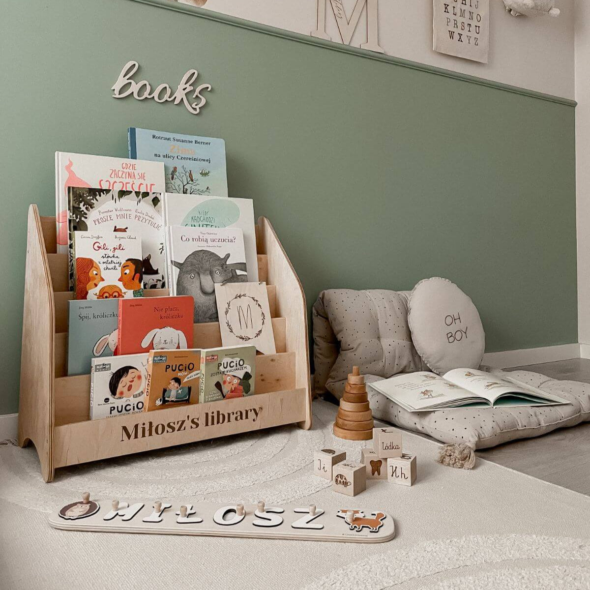 Children's bookshelf with books and toys in a room with a green wall.