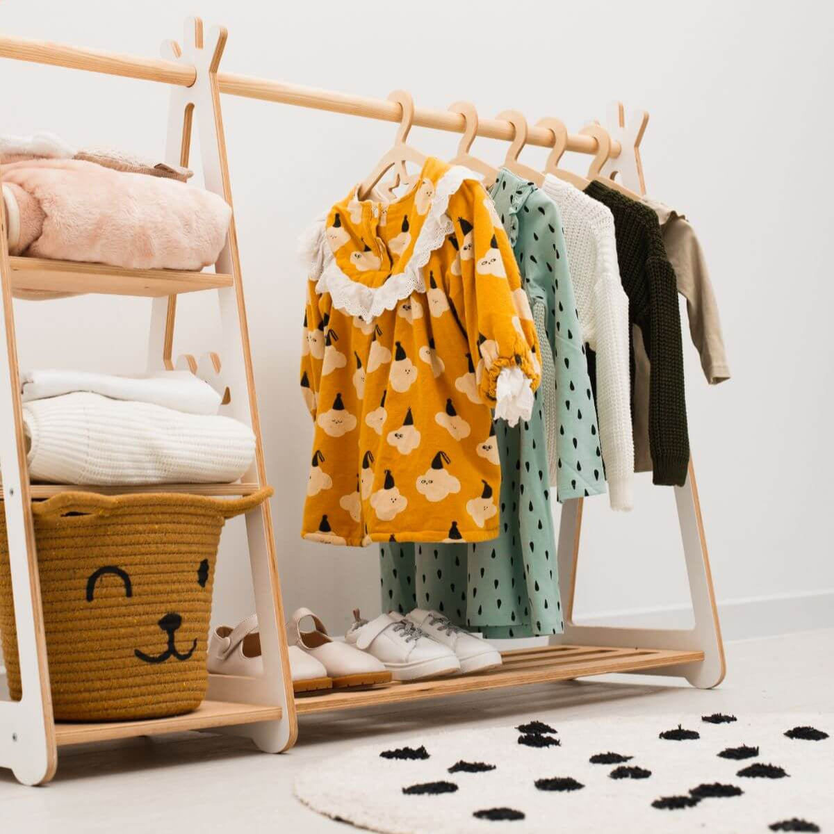 Children's clothing on a wooden rack with a basket and toys in the background
