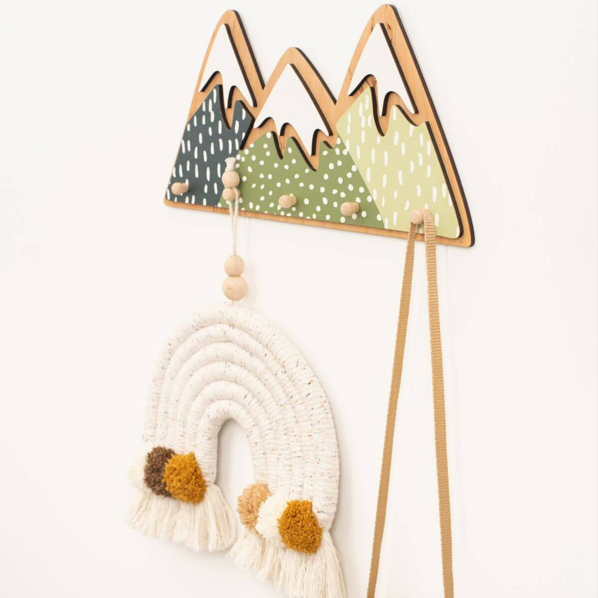 Decorative wall hook with mountain design and hanging macramé wall art on a white background