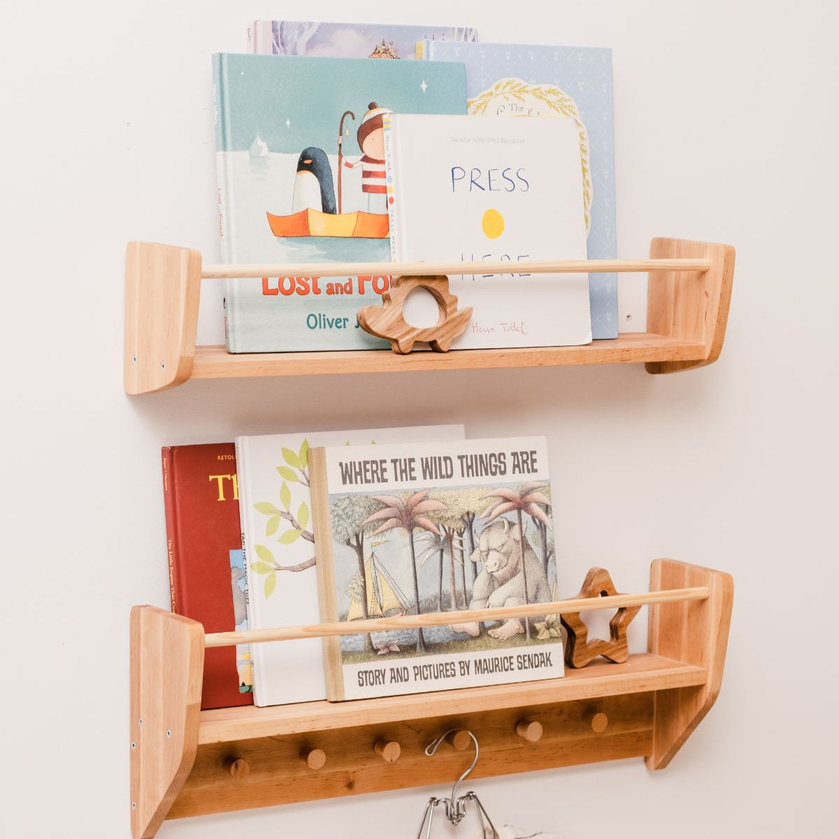 Wooden wall shelf with children's books and decorative items on a white wall.