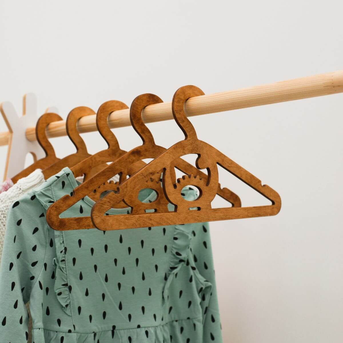 Wooden hangers on a rack with a green dress featuring black patterns.