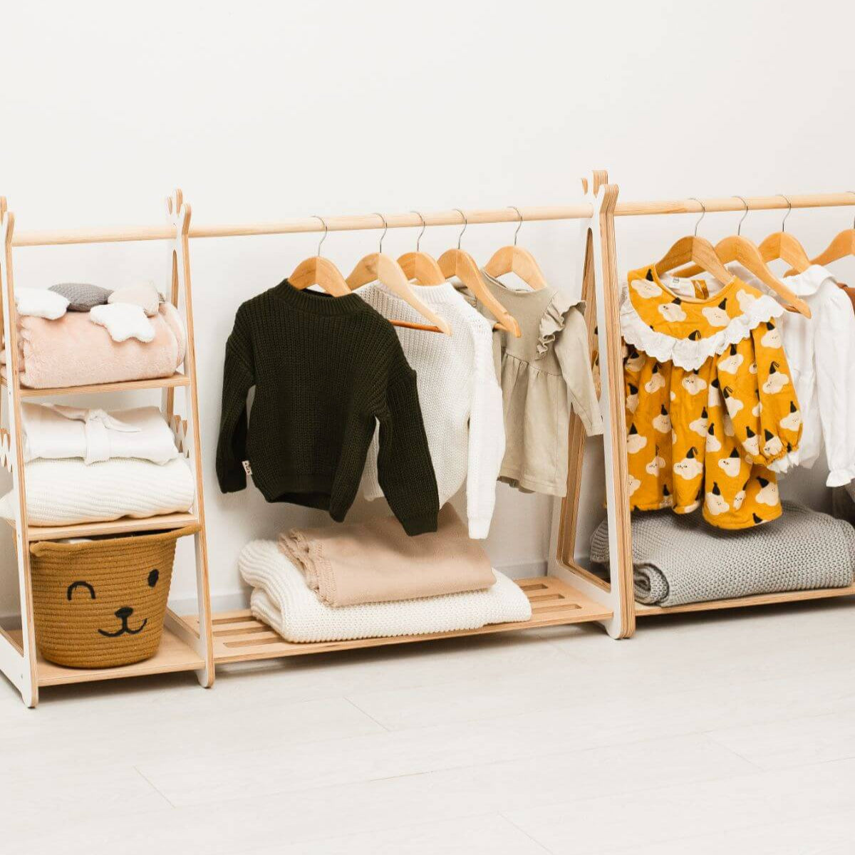 Children's clothing on wooden hangers and shelves against a white wall.