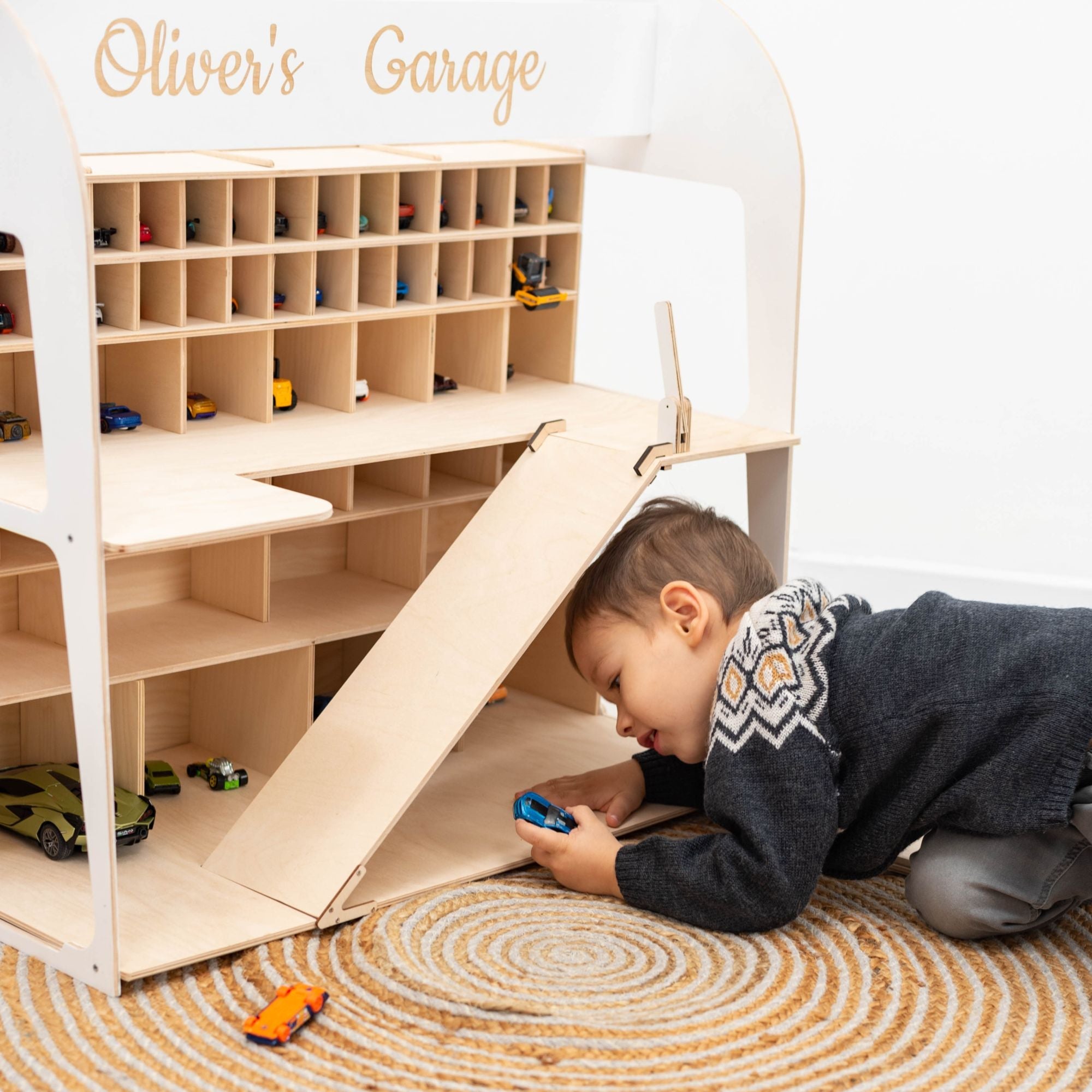 Child playing with a toy garage set up with shelves and a door, labeled 'Oliver's Garage'.
