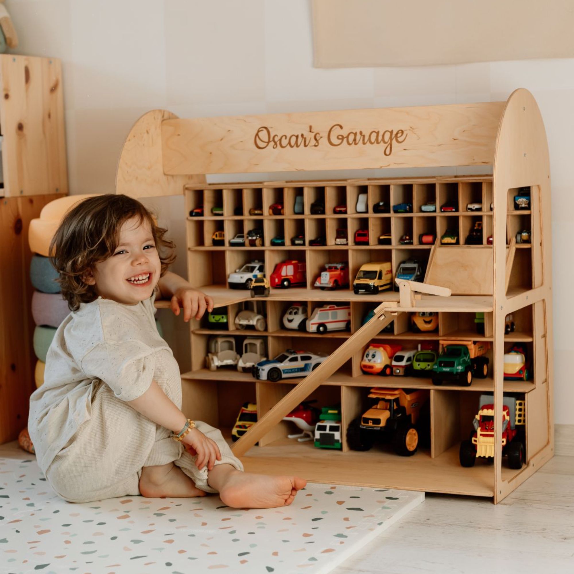 Child playing with a wooden toy garage filled with colorful model cars.