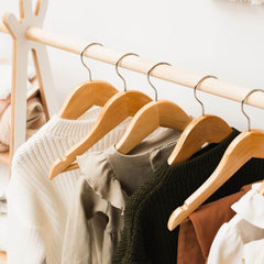 Wooden hangers with clothes on a rack against a neutral background