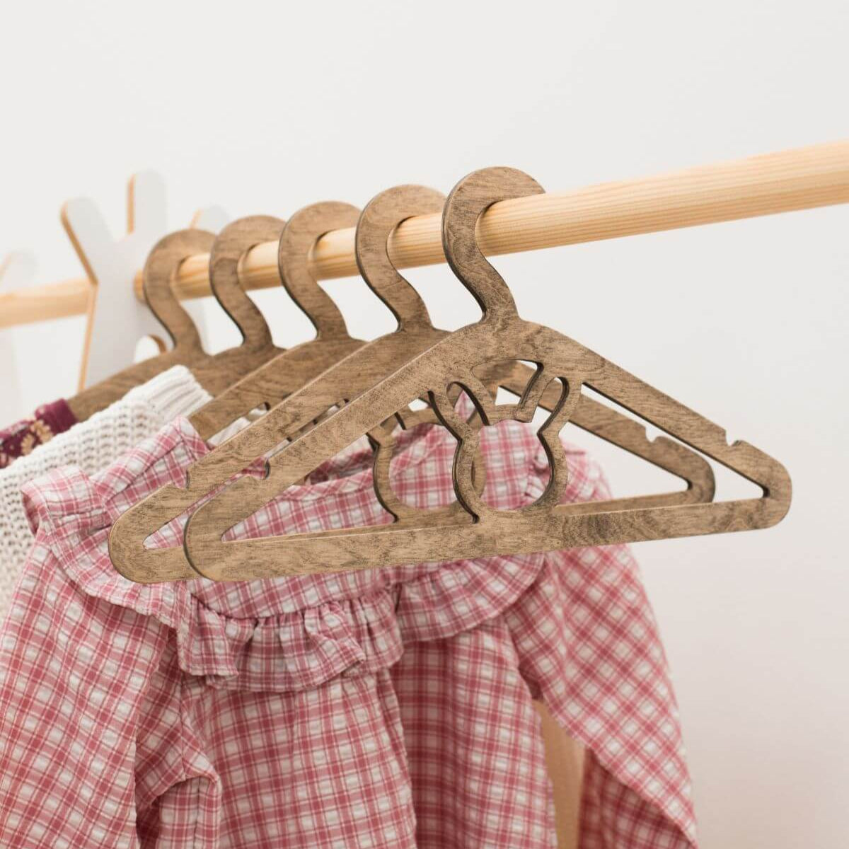 Wooden hangers on a rack with a red and white checkered garment underneath.